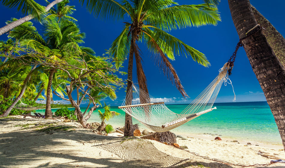 Empty hammock in the shade of palm trees on tropical Fiji Islands (photo via mvaligursky / iStock / Getty Images Plus)