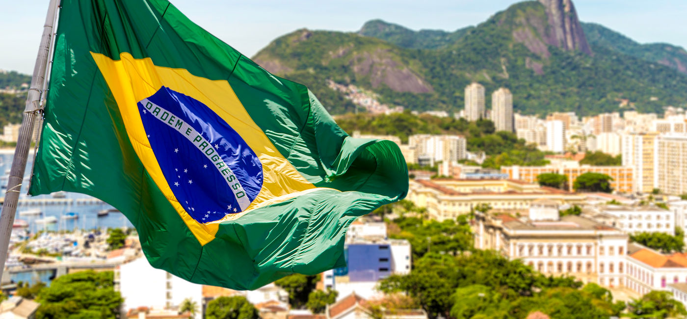 Image: Brazil's national flag waving above Rio de Janeiro. (photo via iStock/Getty Images Plus/filipefrazao)