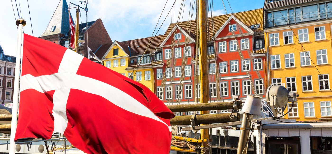 Image: Denmark's national flag flying in the foreground of Copenhagen's famous old Nyhavn port. (photo via iStock/Getty Images Plus/nantonov)