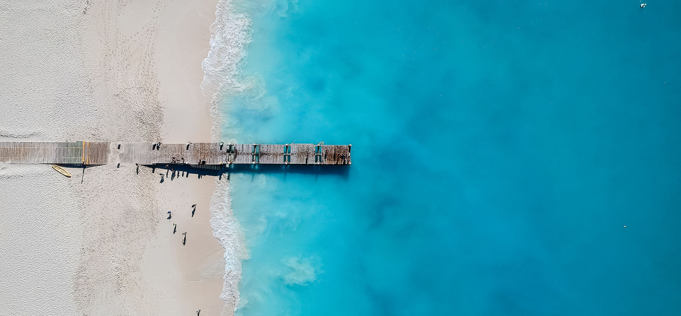 Image: Drone photo of pier in Grace Bay, Providenciales, Turks and Caicos. The caribbean blue sea and white sandy beaches can be seen (photo via JoaoBarcelos / iStock / Getty Images Plus)