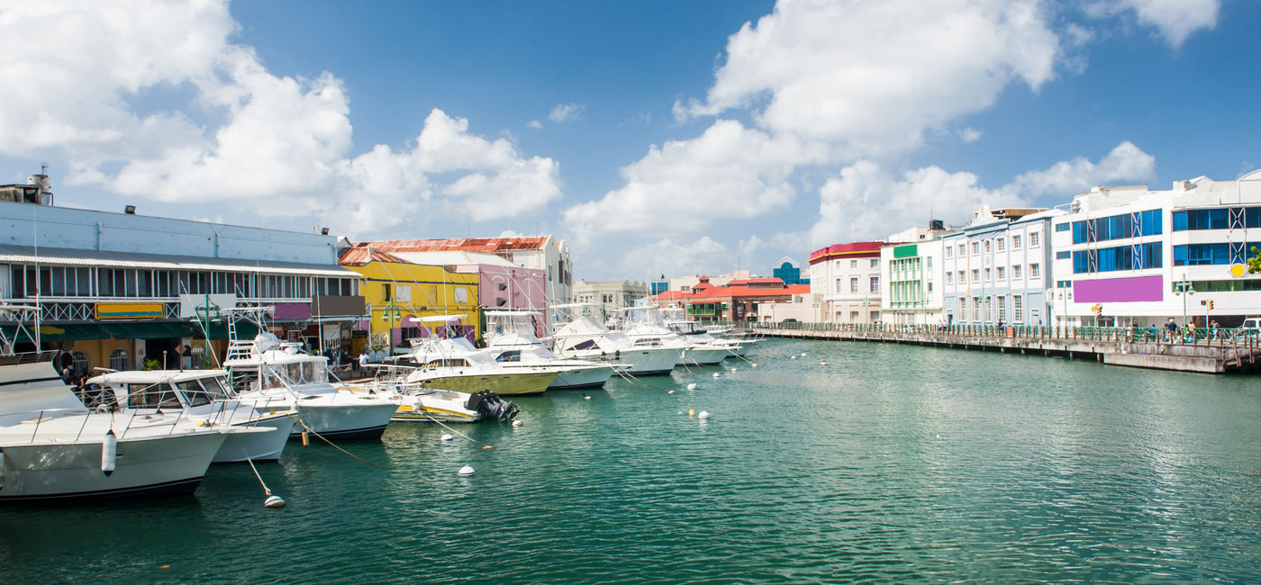 Image: Main water canal with ships and shops in Bridgetown, capital of Barbados. Caribbean (photo via Fyletto / iStock / Getty Images Plus)