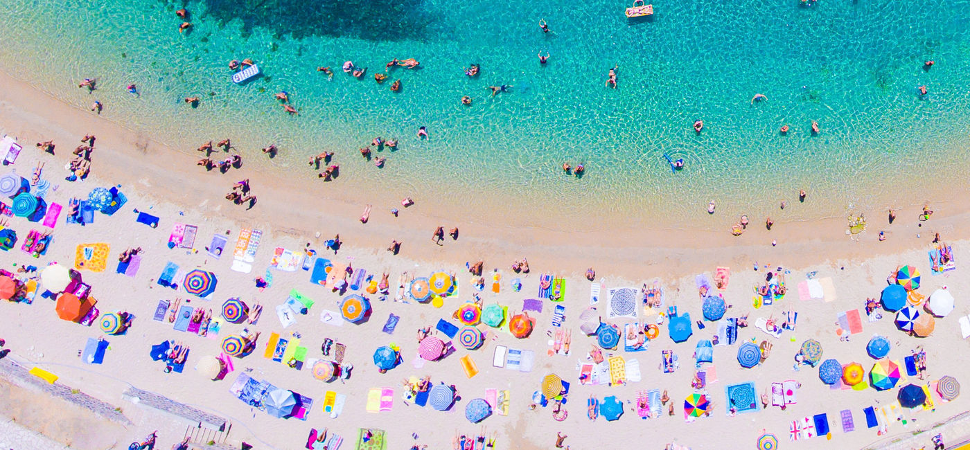 Image: People bathing in the sun at the beach, aerial view with clear blue water and sandy beach. Corfu island Kerkyra, Greece (photo via CalinStan/iStock/Getty Images Plus)
