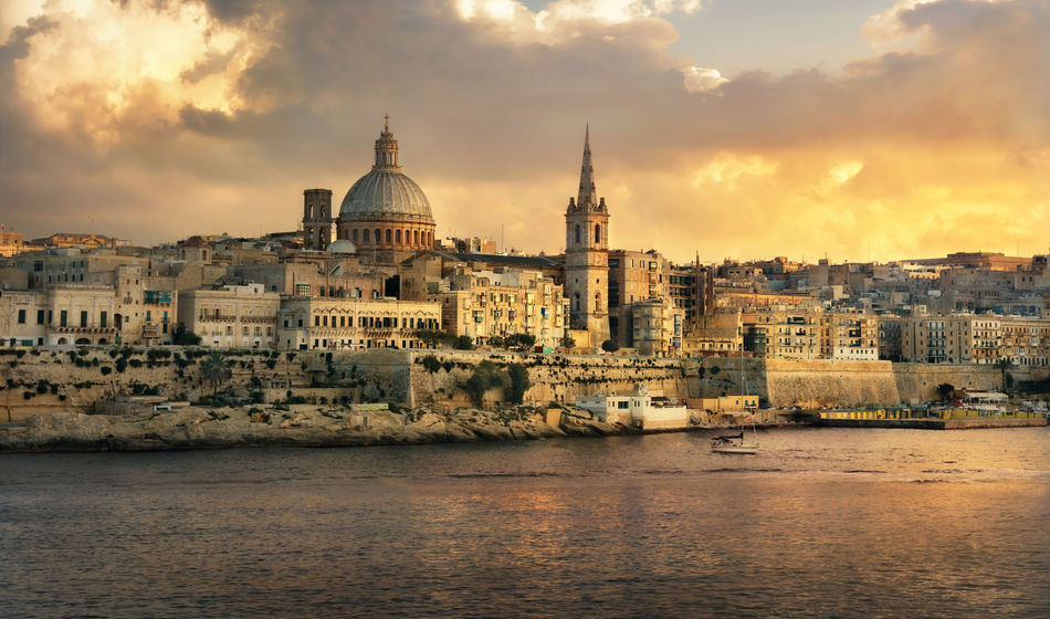 Panoramic view of Valletta at sunset with Carmelite Church dome and St. Pauls Anglican Cathedral. Malta (photo via Bareta / iStock / Getty Images Plus)