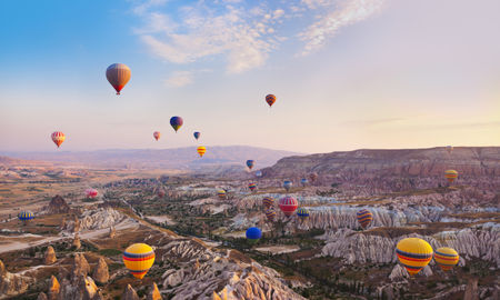 Hot air balloon flying over rock landscape at Cappadocia Turkey (photo via TPopova / iStock / Getty Images Plus)